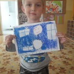 Chłopiec przedstawia pracę na której jest narysowany na tle domu