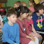 Dzieci siedzą na ławce i zainteresowaniem oglądają przedstawienie